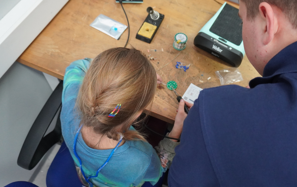 Kind lötet elektronische Bauteile mit Unterstützung bei einem Elektronikprojekt