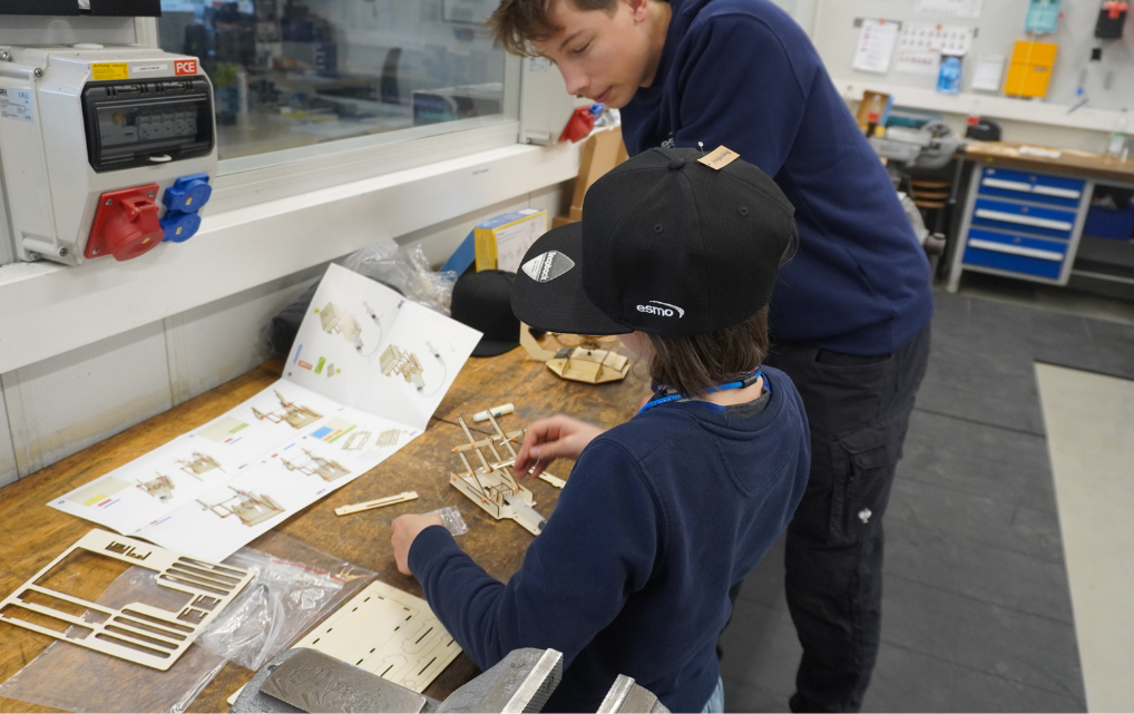 Kind erhält Unterstützung beim Zusammenbau eines Holzbausatzes in der Lehrwerkstatt