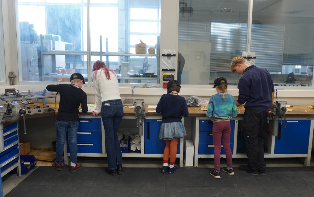 Kinder und Betreuungspersonen arbeiten gemeinsam an Werkbänken während des Kids Day