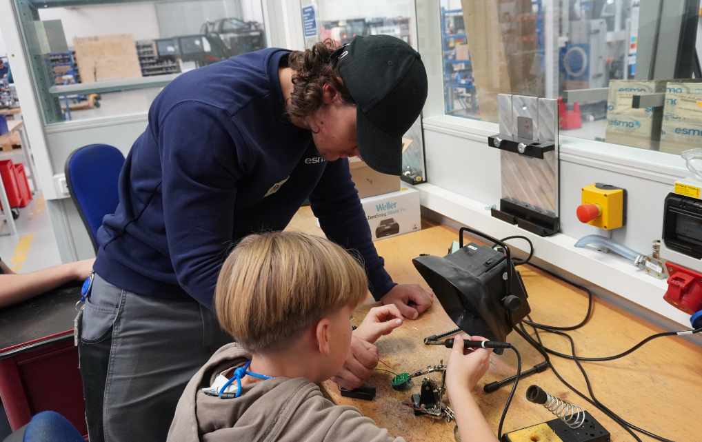 Kind lötet Bauteile mit Unterstützung eines Mitarbeiters in der Elektronikwerkstatt