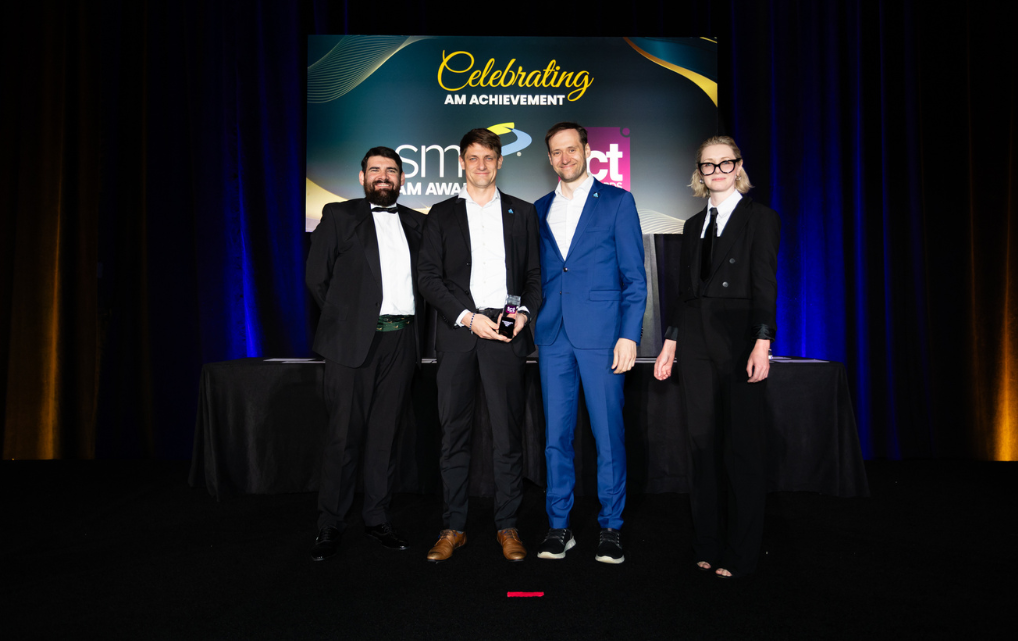 Preisverleihung TCT Hardware Award: Vier Personen auf der Bühne mit Trophäe vor dem Schriftzug „Celebrating AM Achievement"