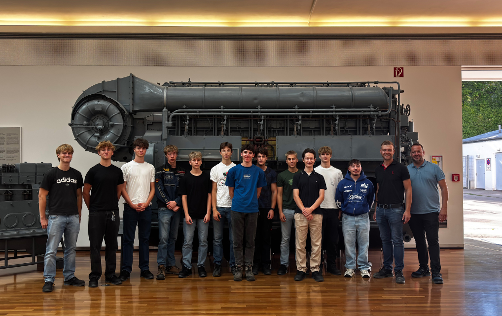 Gruppe der esmo-Auszubildenden und Begleitpersonen vor einem großen Dieselmotor im MAN Museum in Augsburg.