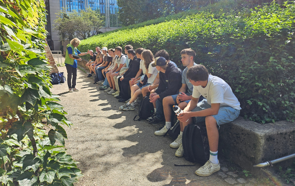 Azubi-Gruppe der esmo group sitzt im Park und hört der Stadtführerin zu.