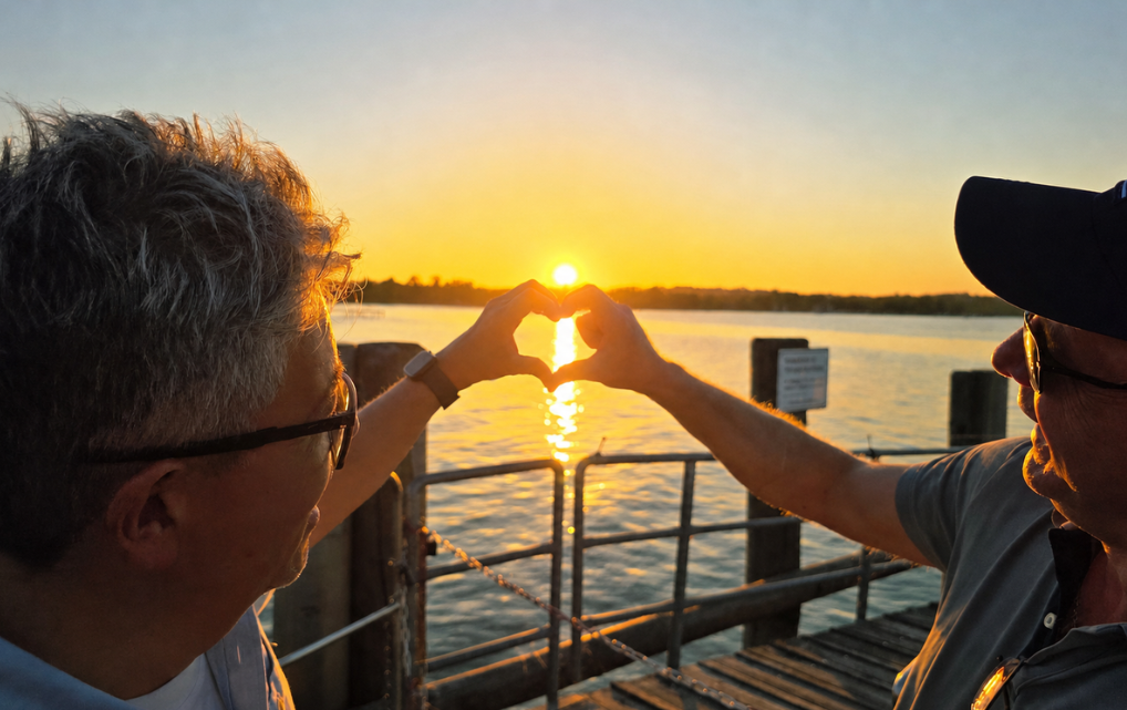 Two esmo colleagues forming a heart with their hands at sunset by the lake.