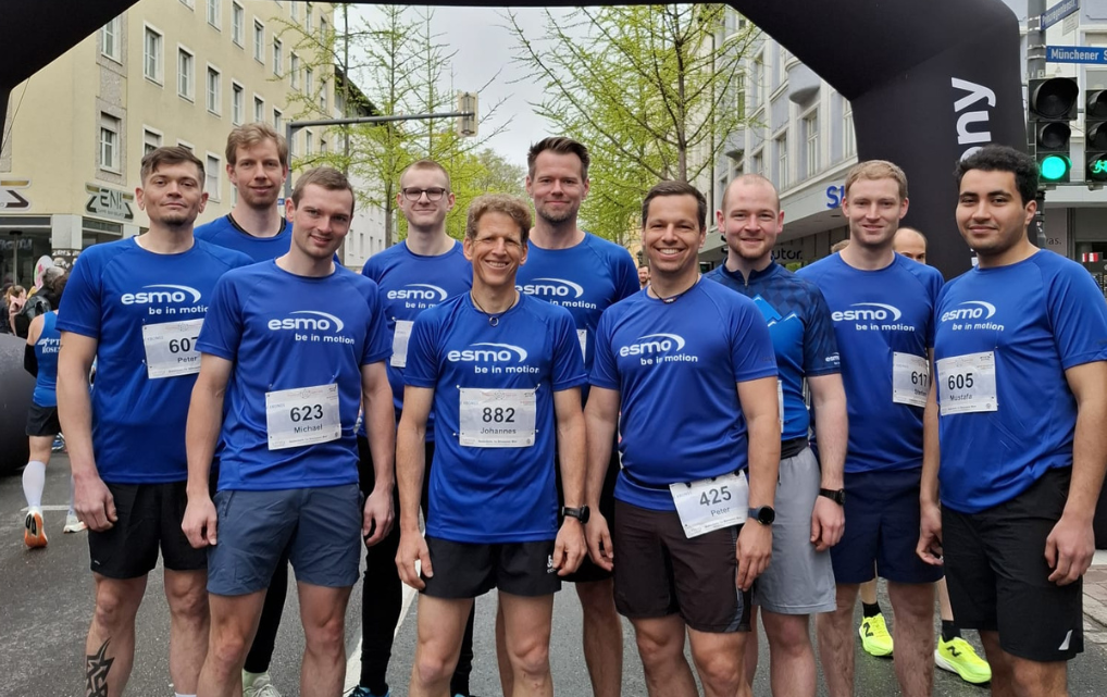 Gruppenfoto von 10 Läufern im esmo-Shirt vor dem Startbogen beim Rosenheimer Citylauf in der Innenstadt.