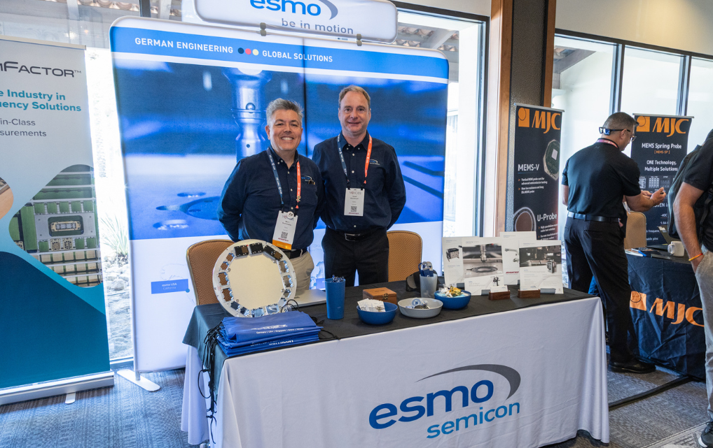 Josef Weinberger (Deutschland) und Bert Bustamante (USA) am esmo semicon Messestand auf der ADVANTEST Voice im Mai 2026 in Scottsdale, Arizona. Große Präsentationswand mit dem Slogan „German Engineering – Global Solutions". Auf dem Messetisch verschiedene Halbleiter-Handling-Komponenten, darunter kreisförmige Systeme und technische Bauteile. Rechts im Hintergrund der MJC-Stand.