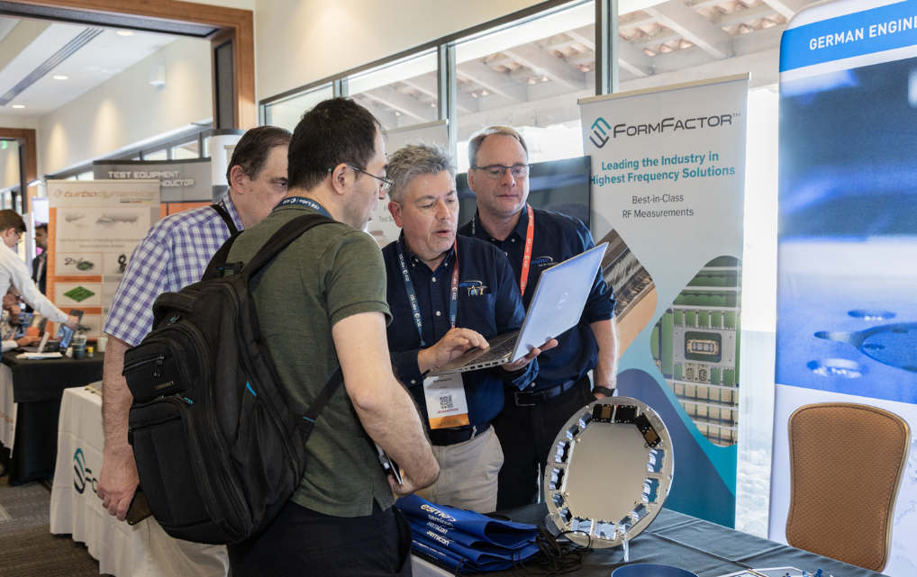 Josef Weinberger and Bert Bustamante presenting semiconductor handling systems at the esmo semicon booth at ADVANTEST Voice in May 2026 in Scottsdale, Arizona. Trade show visitors examining a circular handling system on the exhibition table. Booth walls with FormFactor branding and RF measurement technology information visible in the background.