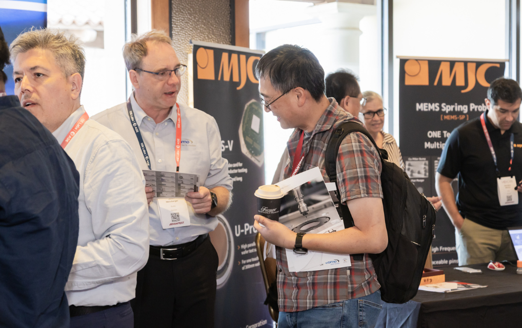 Josef Weinberger (esmo, Deutschland) und Bert Bustamante (esmo, USA) im Gespräch mit Messebesuchern am esmo semicon Stand auf der ADVANTEST Voice im Mai 2026 in Scottsdale, Arizona. Im Vordergrund Bert Bustamante in hellem Hemd mit Broschüren, dahinter Messebesucher. Im Hintergrund weitere Messestände, darunter MJC.