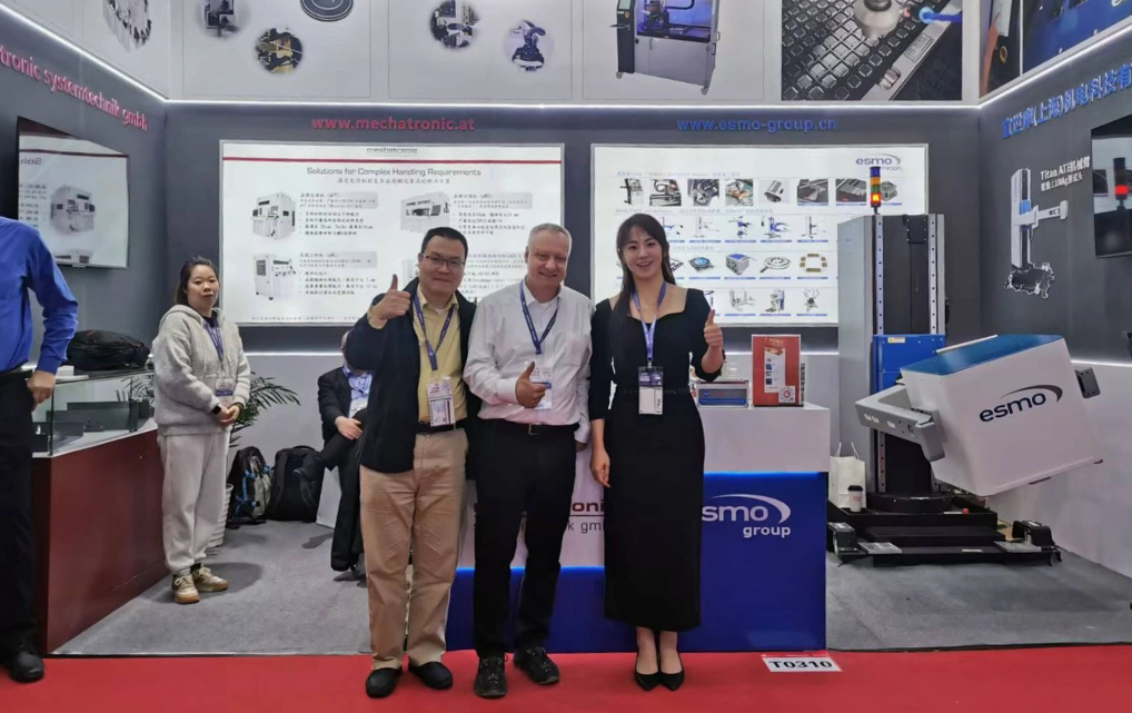 Drei Teammitglieder von esmo und mechatronic am Messestand T0310 auf der SEMICON China 2026 – im Hintergrund der Titan1100 Autosetup Manipulator und das esmo group-Banner