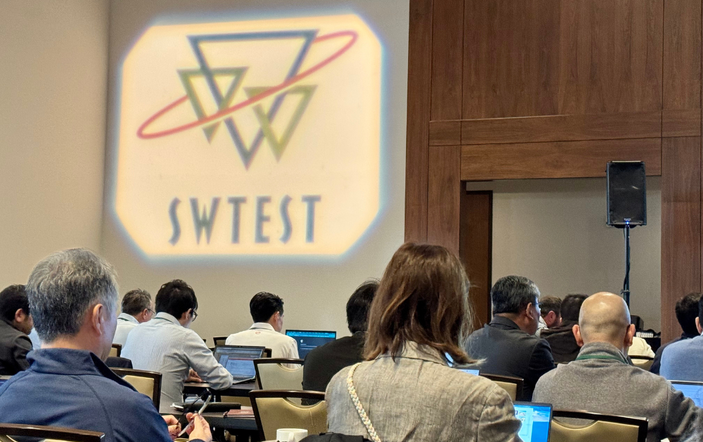 Konferenzteilnehmer verfolgen eine Präsentation während der SWTest 2025; im Hintergrund ist das beleuchtete Logo der Veranstaltung sichtbar.